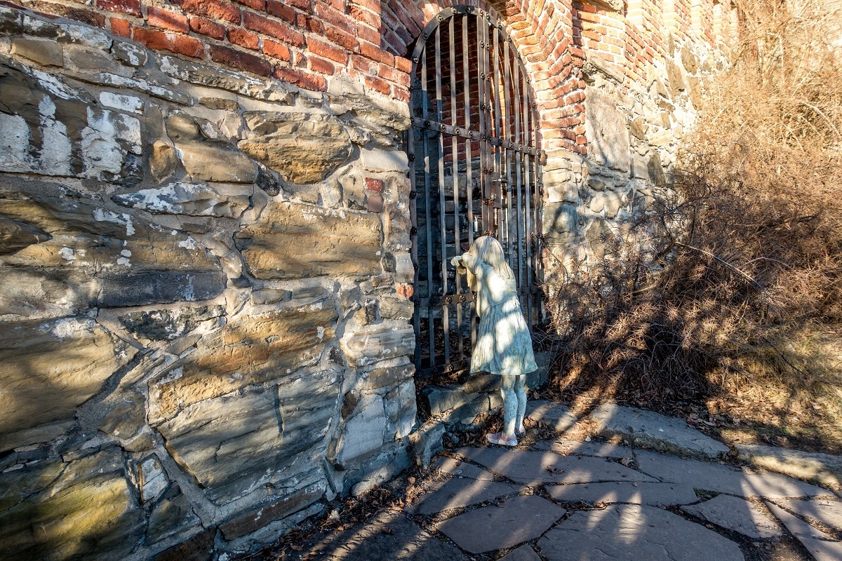 Statue of young girl peering through a gate