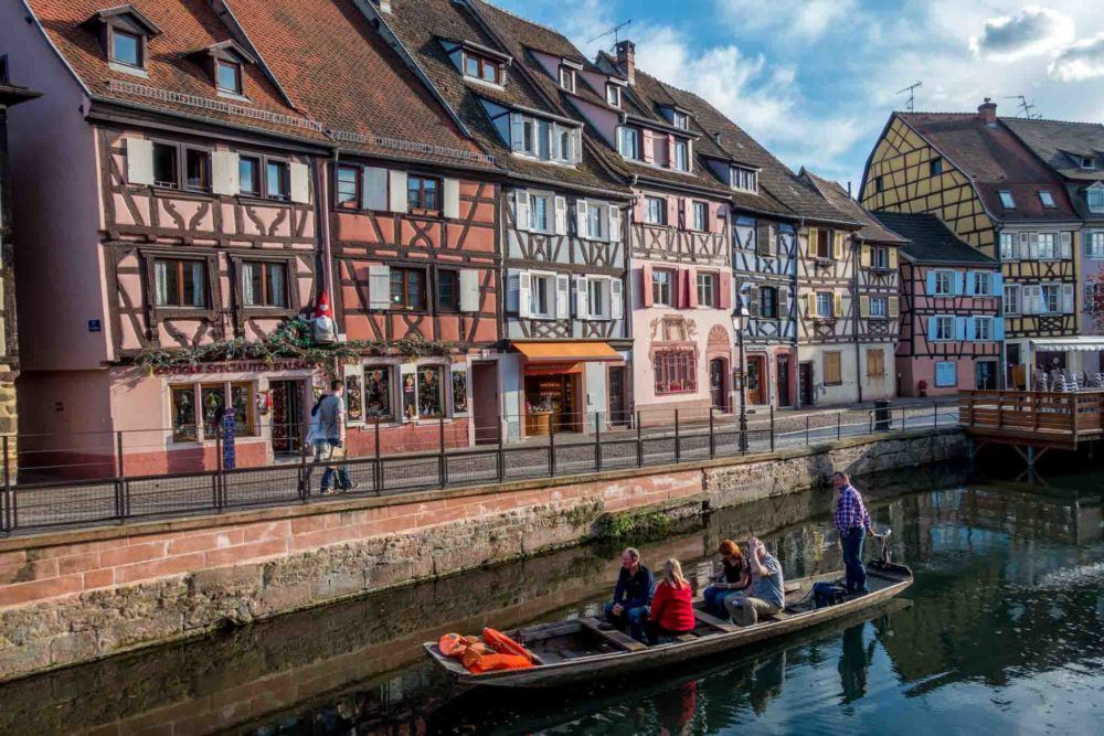 People in a boat passing brightly colored half-timber buildings