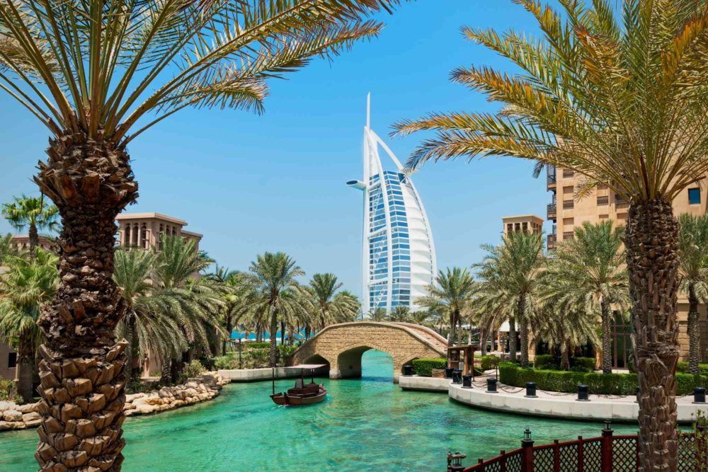 White sail-shaped building with water and palm trees