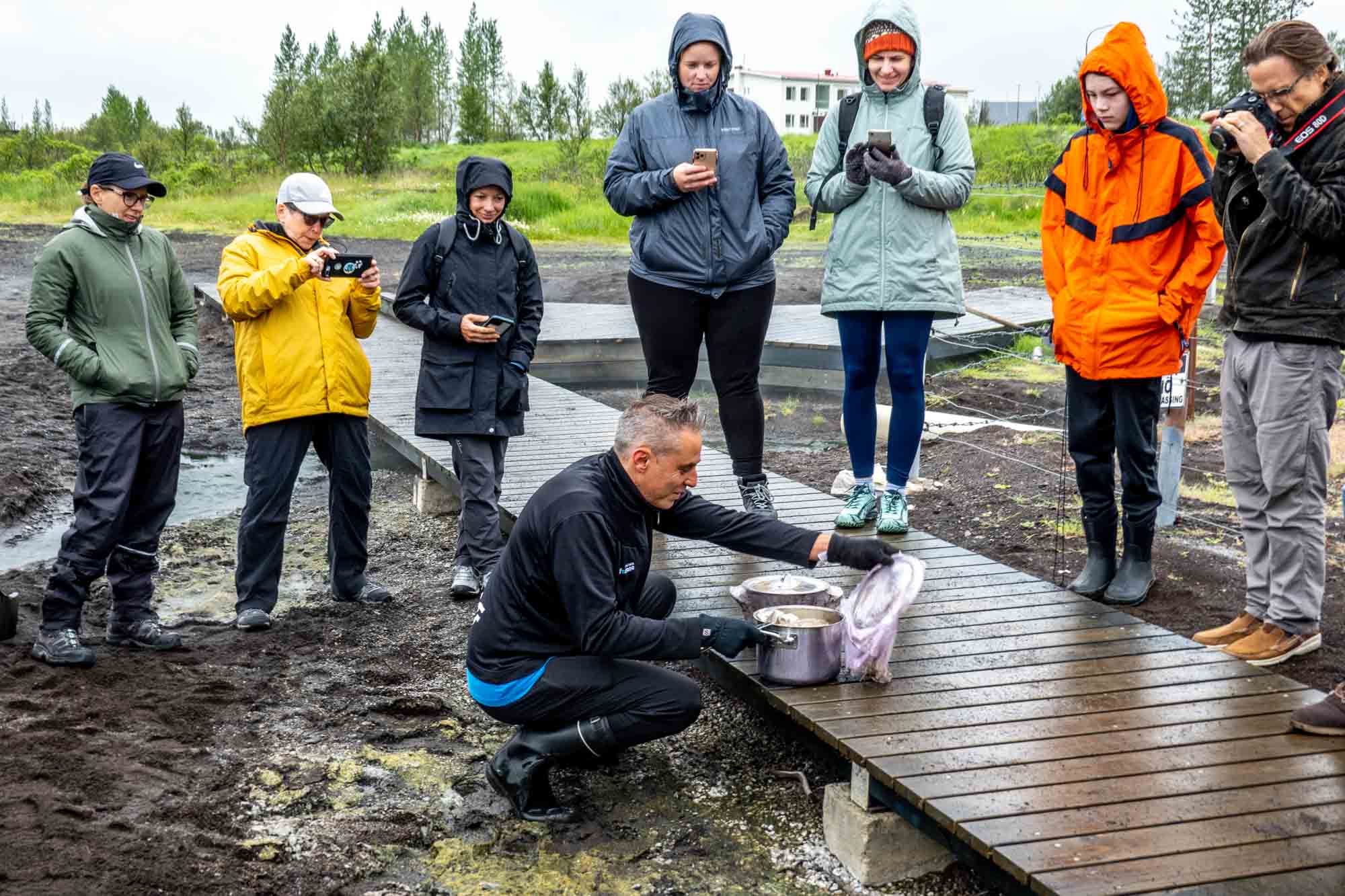 People watching a man open a pot on a black sand beach