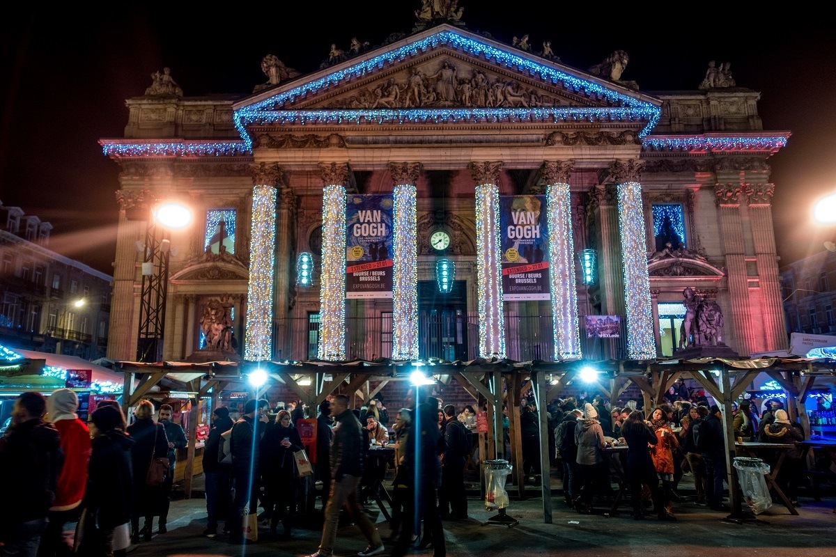 Visitors to market stalls in front of large building with columns.