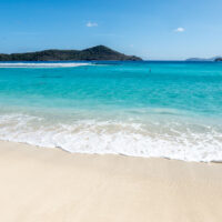 Blue ocean water and a white sand beach with hilly islands in the distance in St. Thomas