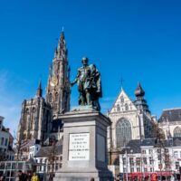 City square surrounded by cafes and a cathedral with a statue of a man at the center