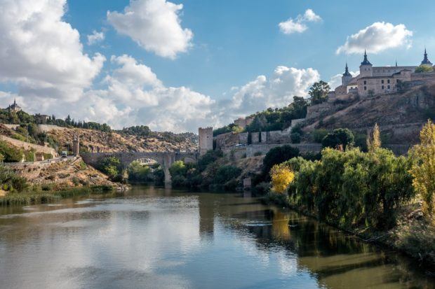 Stone bridge over a river beside a castle on a hill