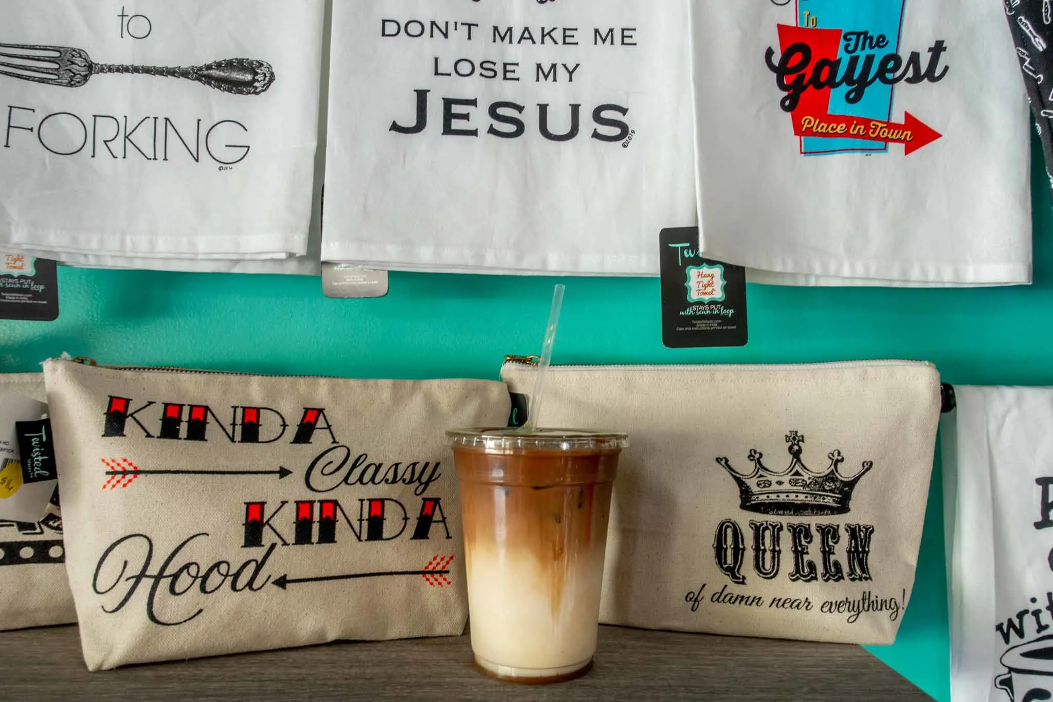 Coffee drink on shelf surrounded by bags and hand towels.