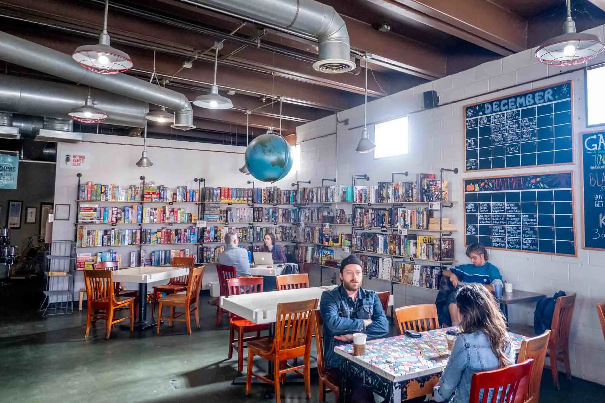 People at tables by a wall of board games.
