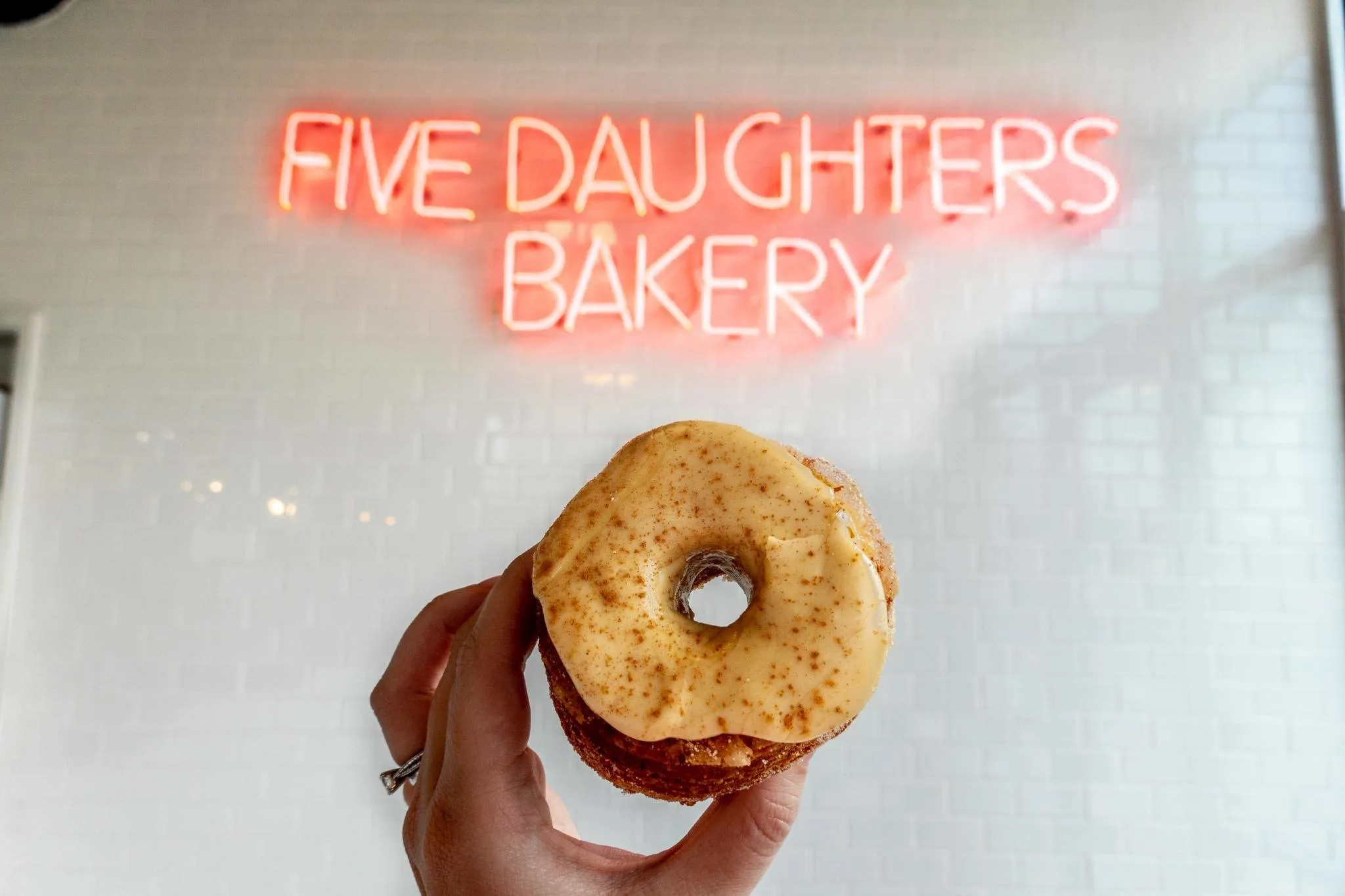 Maple glazed donut under the illuminated Five Daughters Bakery sign.