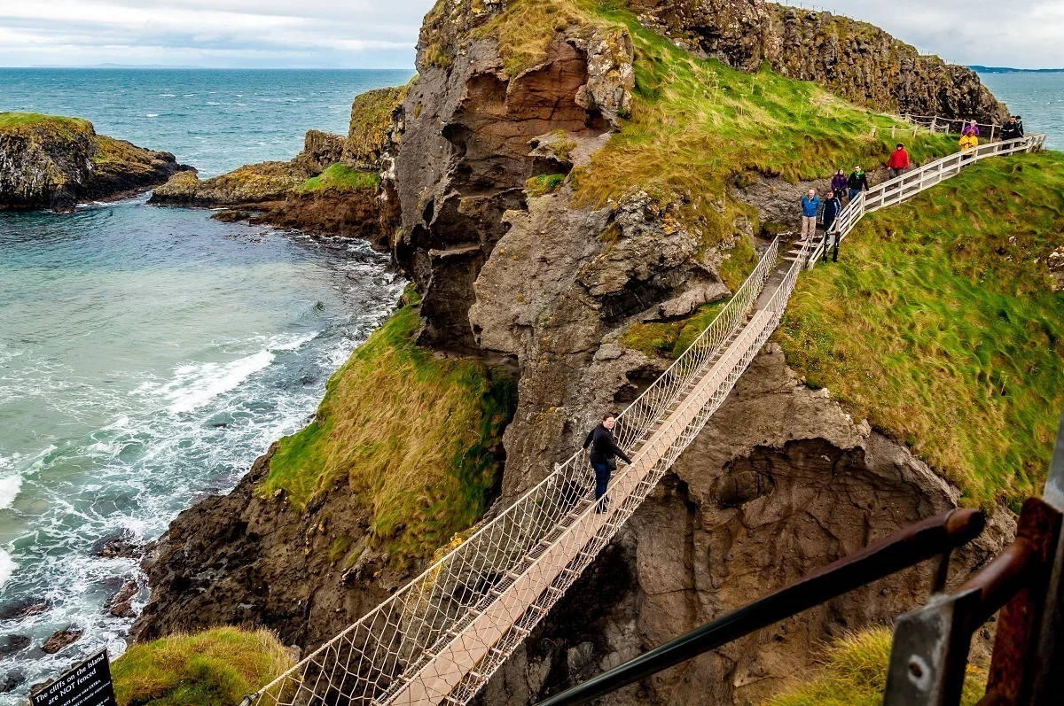 People crossing a rope bridge above the ocean