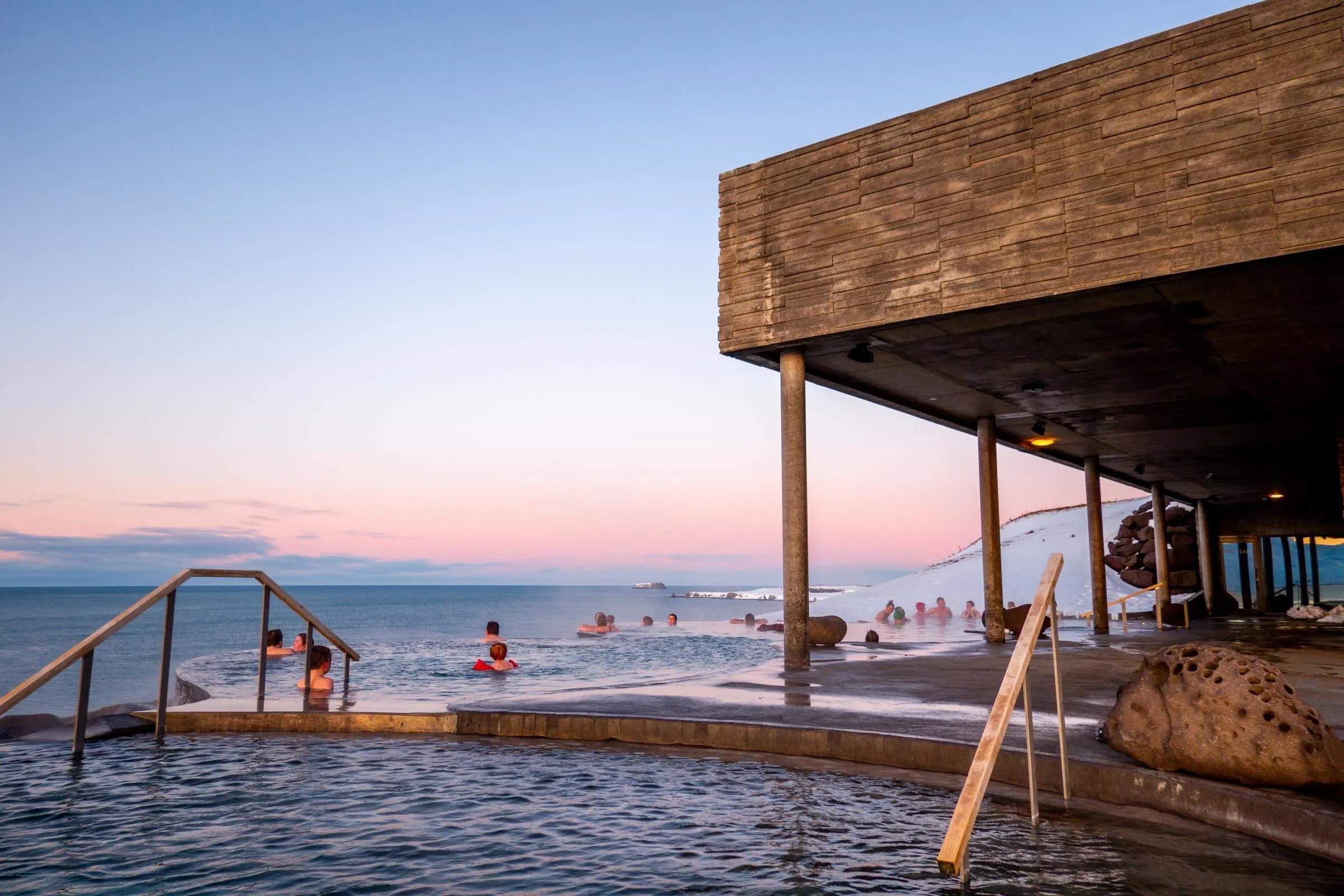 People in pools overlooking the ocean at sunset